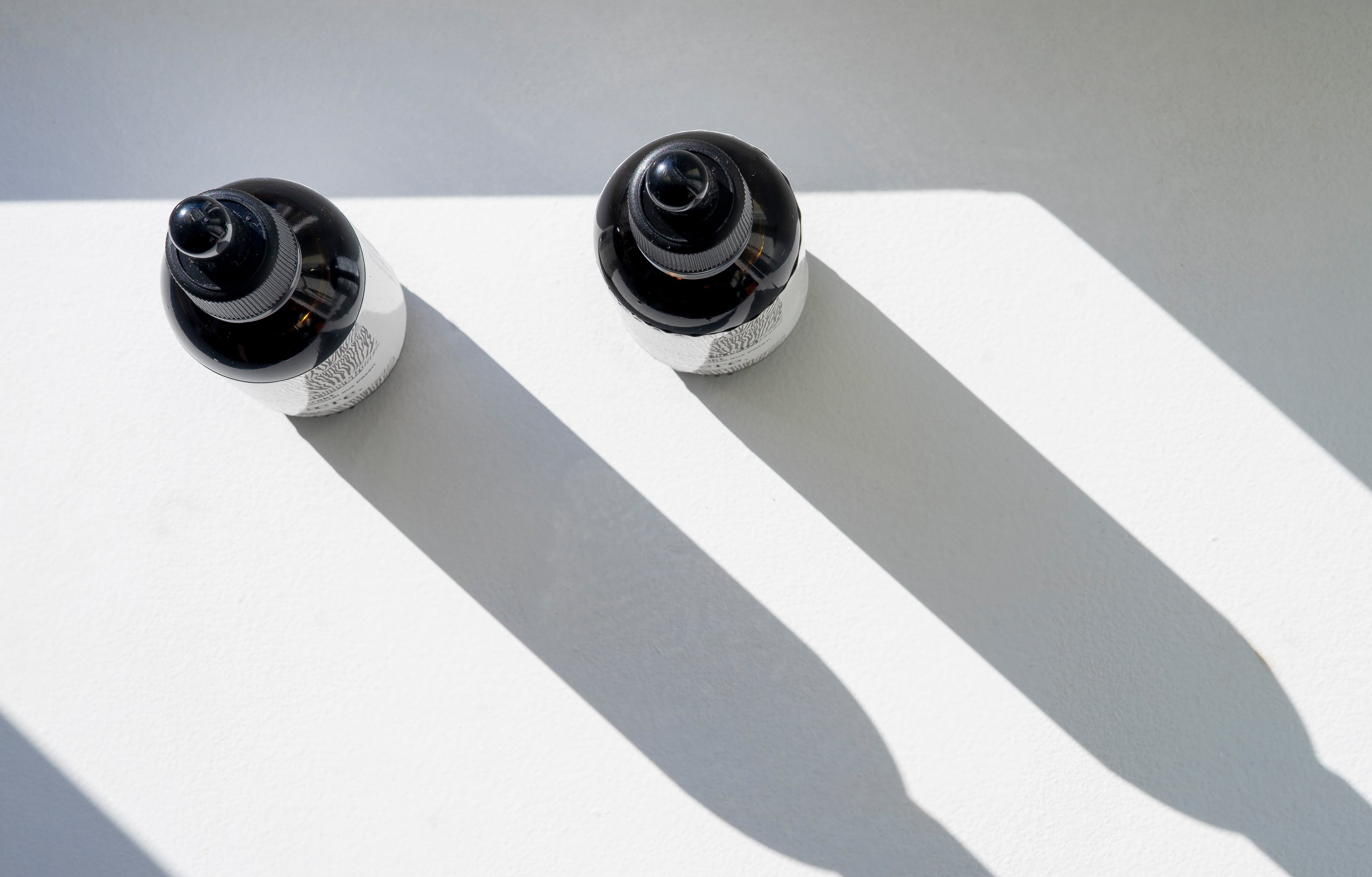 Zwei CBD Öl Fläschchen von Velvaere mit langen Schatten auf weißem Hintergrund – minimalistisches Produktfoto